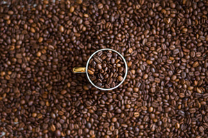 a coffee mug full of coffee beans above more coffee beans